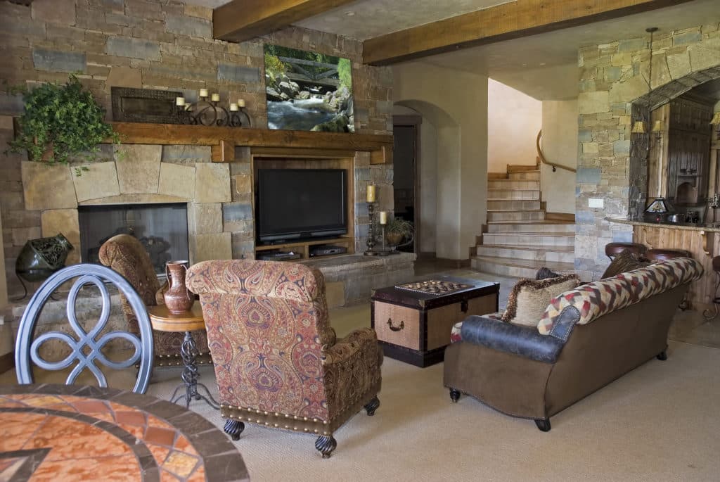 Cozy living room with stone walls, a fireplace, a television, and stylish furniture, showcasing potential ideas for modern basement remodeling and enhancing livable space.