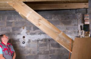 Man Wearing Vest Standing in Unfinished Basement Inspecting Work on Wooden Staircase Inside New Home Construction Site