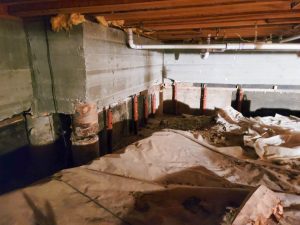 Crawl space interior showing moisture control measures, including support beams and protective coverings, relevant to basement waterproofing solutions.