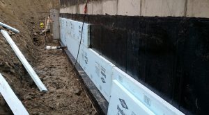 Foundation waterproofing installation with black sealant and insulation panels, showcasing essential techniques for basement moisture control and protection.