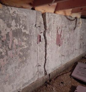 Cracked basement wall with visible damage and exposed foundation, illustrating the need for professional basement waterproofing and repair services.