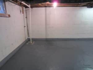 Clean, dry basement interior with a concrete floor, drainage pipe, and minimal lighting, illustrating effective basement waterproofing and repair solutions.