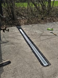 Drainage channel installed in pavement, designed for effective water management, showcasing perforated grates for redirecting water away from foundation, relevant to basement waterproofing solutions.