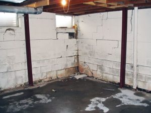 Basement interior showing water damage, cracked walls, and structural I-beams, highlighting issues related to leaky basements and the need for professional repair solutions.