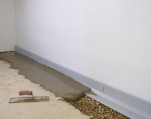 Basement drain tile installation showing a newly poured concrete base with a drainage system along the wall, emphasizing waterproofing solutions for preventing water intrusion.