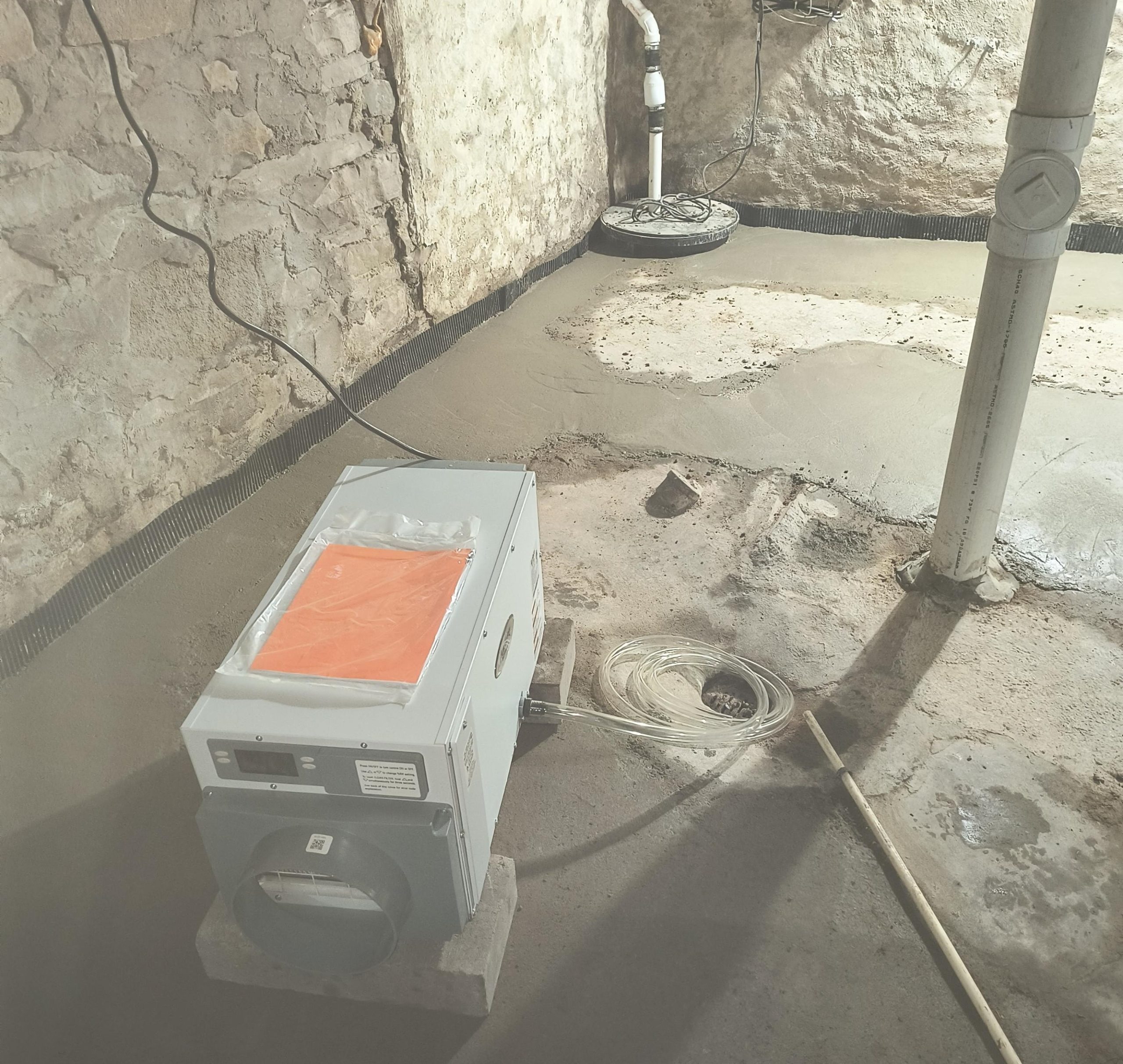 Dehumidifier installed in a basement, surrounded by freshly poured concrete, showcasing moisture management for improved air quality and protection against mold and mildew.