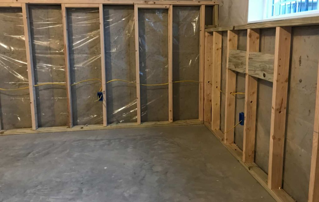 Basement interior showing framed walls with plastic sheeting and electrical wiring, illustrating the preparation for waterproofing and basement repair services.