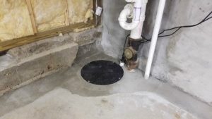 Basement sump pump installation with concrete flooring and drainage system, highlighting waterproofing solutions to prevent water intrusion.