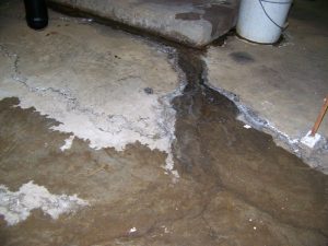 Leaky basement floor with visible water intrusion and cracks, illustrating the need for professional waterproofing services to prevent structural damage.