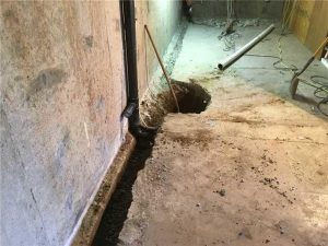 Basement construction site showing a dug-out area for drainage, exposed soil, and tools, illustrating waterproofing and foundation repair processes.