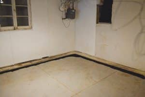 Interior basement waterproofing system featuring a drain tile along the perimeter of a concrete floor, emphasizing water management solutions for preventing moisture infiltration.