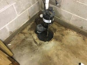 Basement sump pump installation with visible water stains and concrete floor, illustrating the importance of professional waterproofing solutions for preventing water damage.