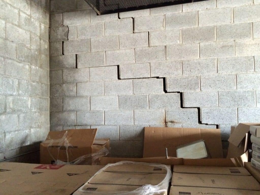 Cracked concrete block wall indicating foundation issues in a basement, surrounded by cardboard boxes, highlighting the importance of timely foundation repair.