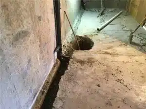 Basement interior showing drainage system installation with a hole in the floor for water management and prevention of moisture issues.