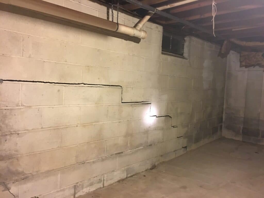 Restoring Home Strength: Proven Foundation Repair Tips Cracked basement wall with visible horizontal and vertical fissures, highlighting potential foundation issues and the need for repair solutions.