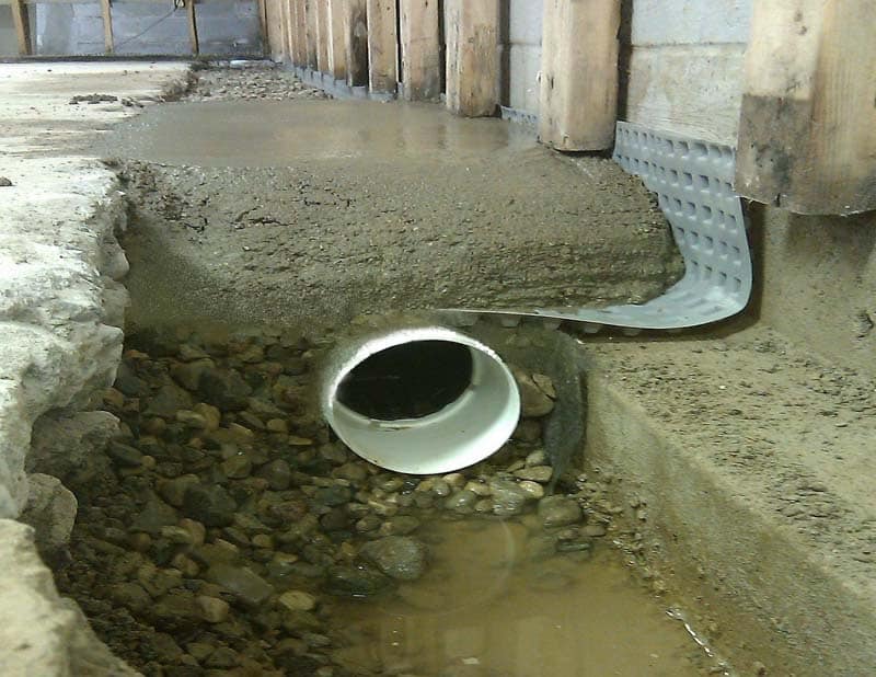 Understanding French Drains in Basement Waterproofing Basement French drain system with perforated pipe, gravel, and concrete, illustrating water diversion for effective waterproofing.