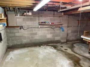 Basement interior showing concrete walls, water pooling on the floor, and shelves, illustrating potential leak issues for waterproofing solutions.