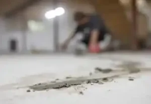 Person applying concrete patch to a basement floor, emphasizing repair techniques for preventing water damage and maintaining a dry environment.