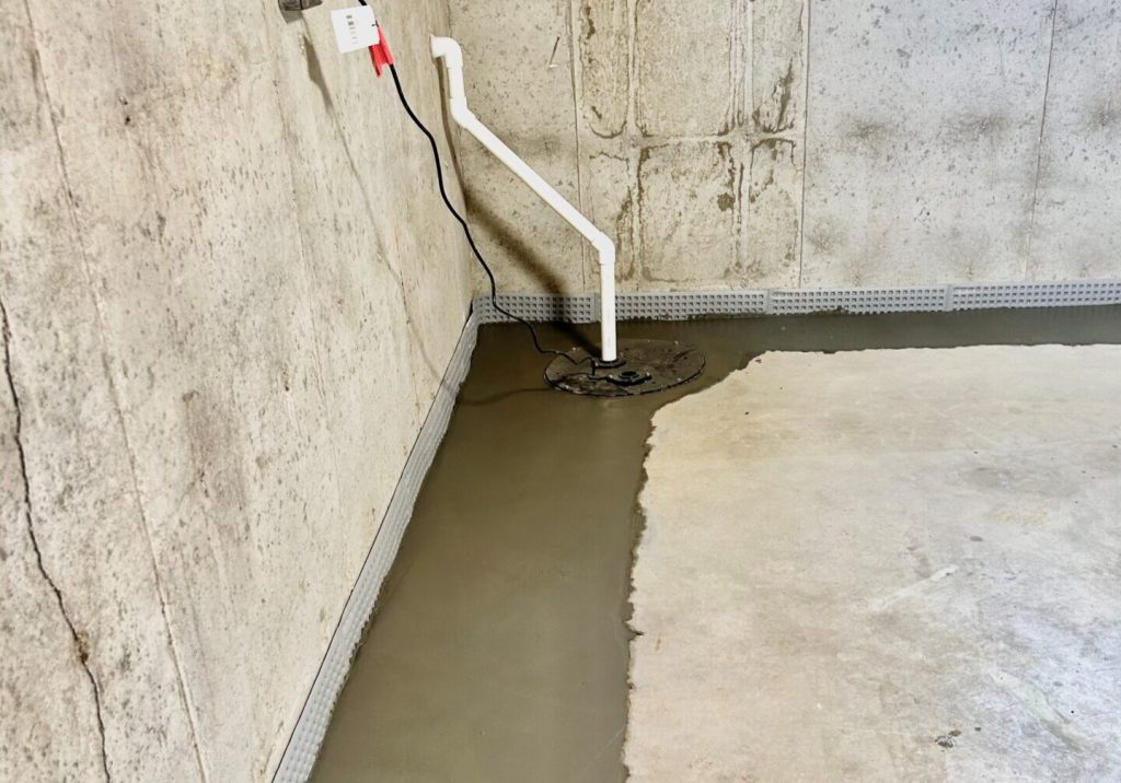 Sump pump installation in a basement with fresh concrete flooring, showcasing waterproofing efforts to prevent water damage.
