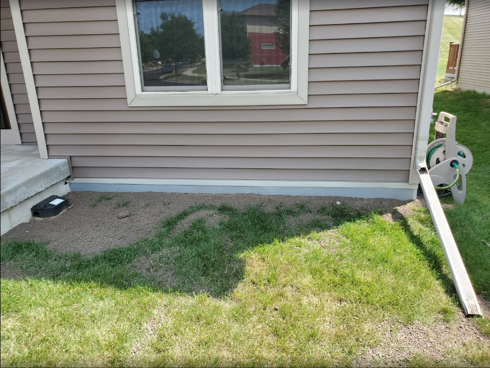 Basement exterior showing a window installation, adjacent to grass and gravel, emphasizing waterproofing and home maintenance for enhanced property value.