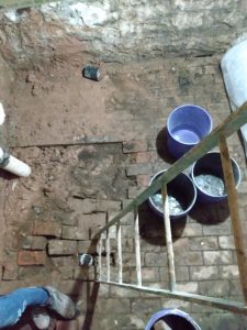 Basement floor with exposed bricks, water pooling in buckets, and a ladder, illustrating potential sources of basement leaks and water damage.