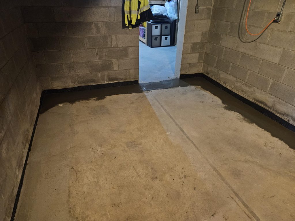 Interior basement with newly installed drain tile system along the perimeter, showcasing concrete floor and cinder block walls, emphasizing waterproofing solutions for storm protection.