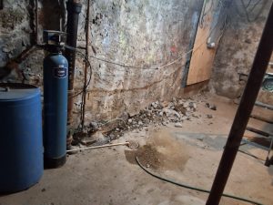 Basement interior showing exposed wall with signs of water damage, cracked foundation, and debris, illustrating potential leak sources and the need for waterproofing solutions.