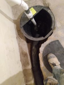 Sump pump installation with drainage pipe in basement, showcasing waterproofing solutions for moisture control and storm protection.