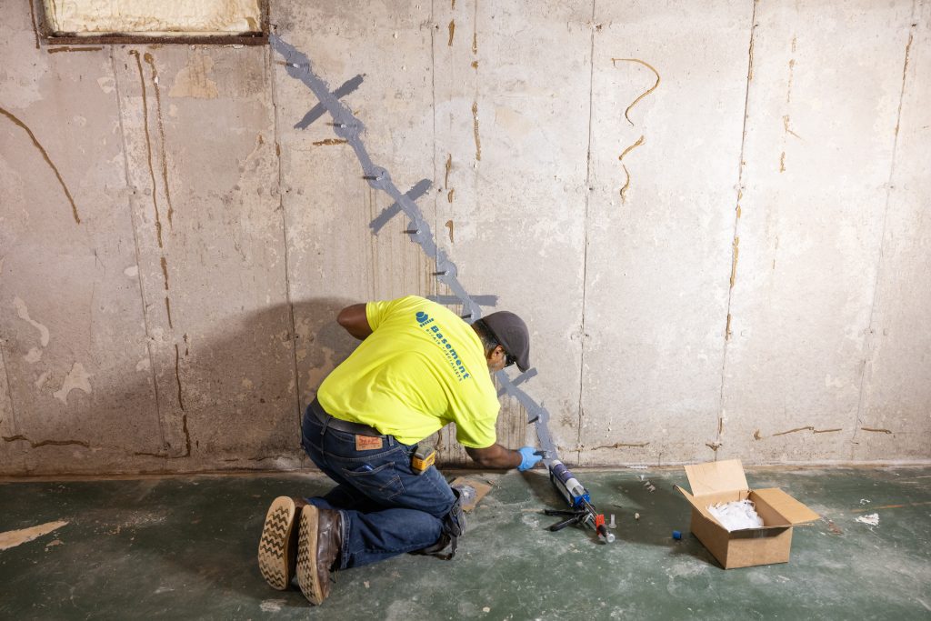 Basement repair technician applying sealant to a foundation crack in a residential basement, highlighting professional foundation repair services by Basement Repair Specialists.