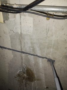 Concrete wall with visible foundation crack repair, gray sealant applied, electrical wires above, indicating structural maintenance for basement integrity.
