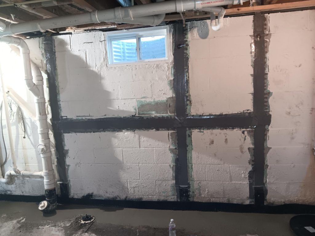 Bowing basement wall with carbon fiber reinforcement, window above, and plumbing visible, illustrating basement repair solutions.