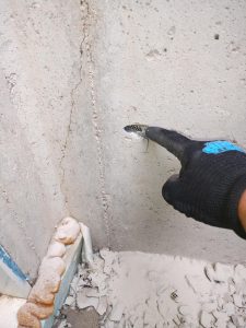 Person pointing at a crack in a concrete wall, demonstrating basement repair techniques and inspection process.