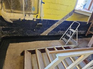 Basement interior showing waterproofing preparation, including painted walls, a ladder, and a floor ready for repairs, highlighting the importance of basement waterproofing techniques.