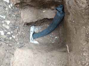 Drainage pipe installation for foundation waterproofing, showcasing trench and black flexible tubing, related to basement repair and prevention of water damage.