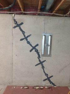 Foundation wall with visible crack repair, featuring sealing material and reinforcement strips, illustrating a method for addressing structural damage in basement repairs.