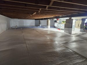 A spacious crawl space with exposed wooden beams and a white insulated floor. Concrete pillars support the ceiling. The area appears clean and organized.