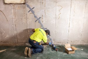 Technician repairing basement wall crack using epoxy injection to prevent water leaks and structural damage