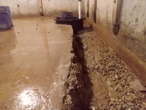 Interior drainage system trench leading to sump pump in wet basement to prevent flooding and water damage