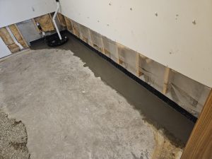 Basement waterproofing system with interior drain tile and sump pump preventing water seepage along foundation wall